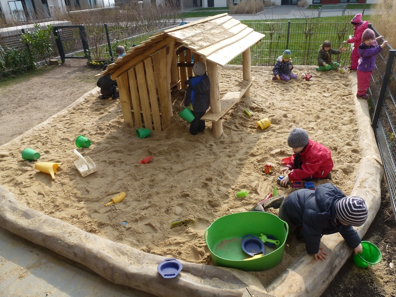Kinder spielen im neuen Sandbereich rund um das fertige Spielhaus